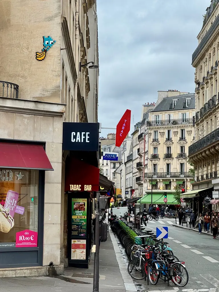 Une œuvre d’invader représentant un Space Invaders tenant des bananes. L’œuvre est au coin d’une rue, au-dessus d’un bar tabac.