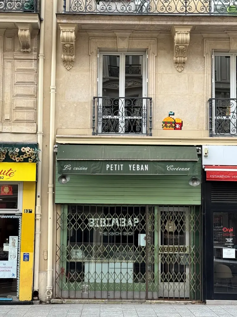 Une œuvre d’invader représentant un Space Invaders tenant des bananes. L’œuvre est au coin d’une rue, au-dessus d’un bar tabac.